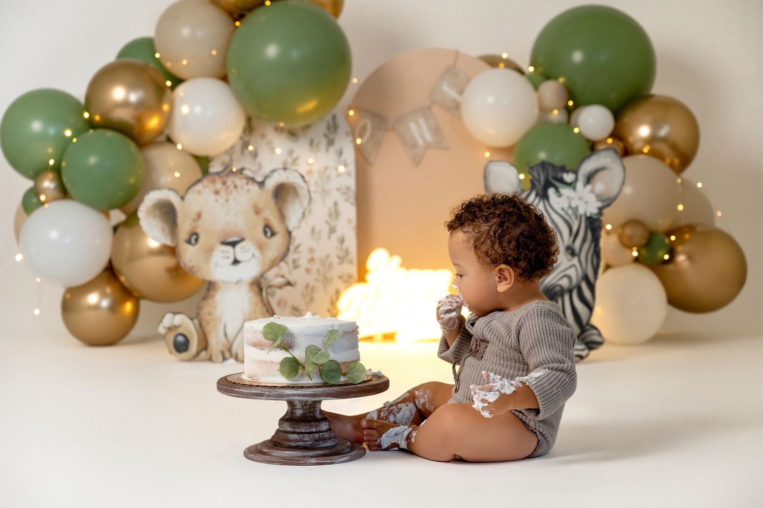 Baby's first birthday cake smash with safari theme, green and gold balloon arch, and jungle animal decorations.