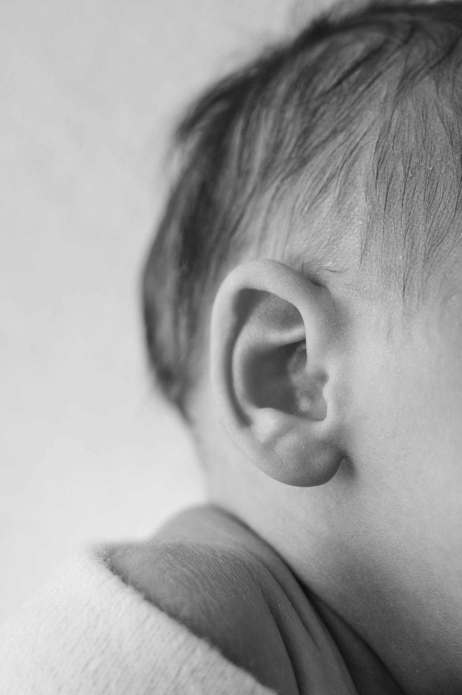 Close-up black and white photo of a baby's ear and soft hair, capturing delicate newborn features.