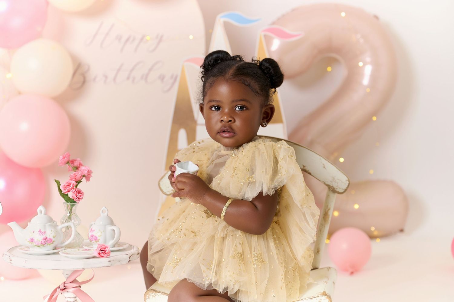 Toddler girl in yellow tulle dress at a pink birthday party with balloons and a number 2, celebrating her 2nd birthday.