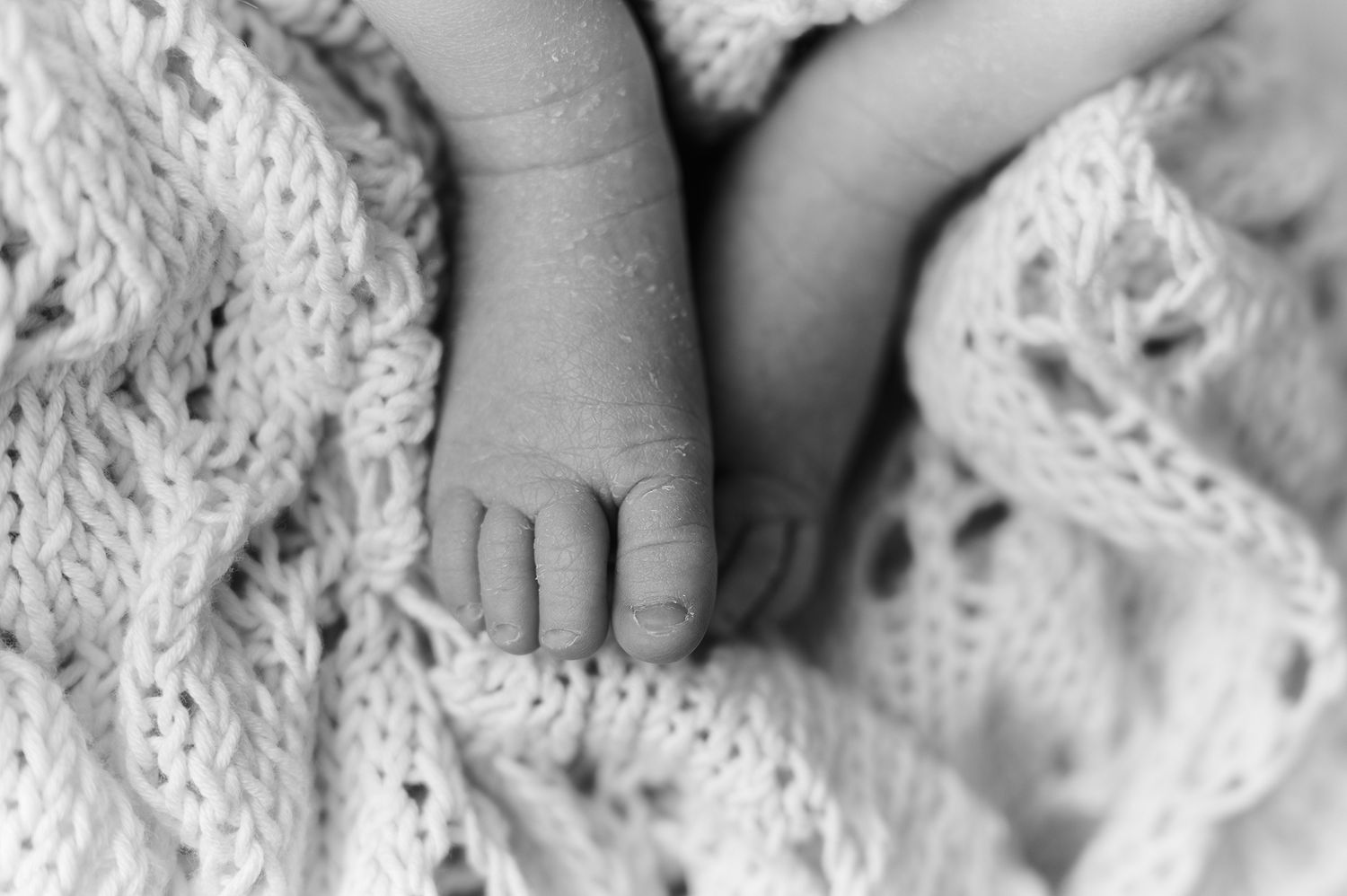Close-up black and white photo of tiny newborn baby feet resting on a soft knit blanket.