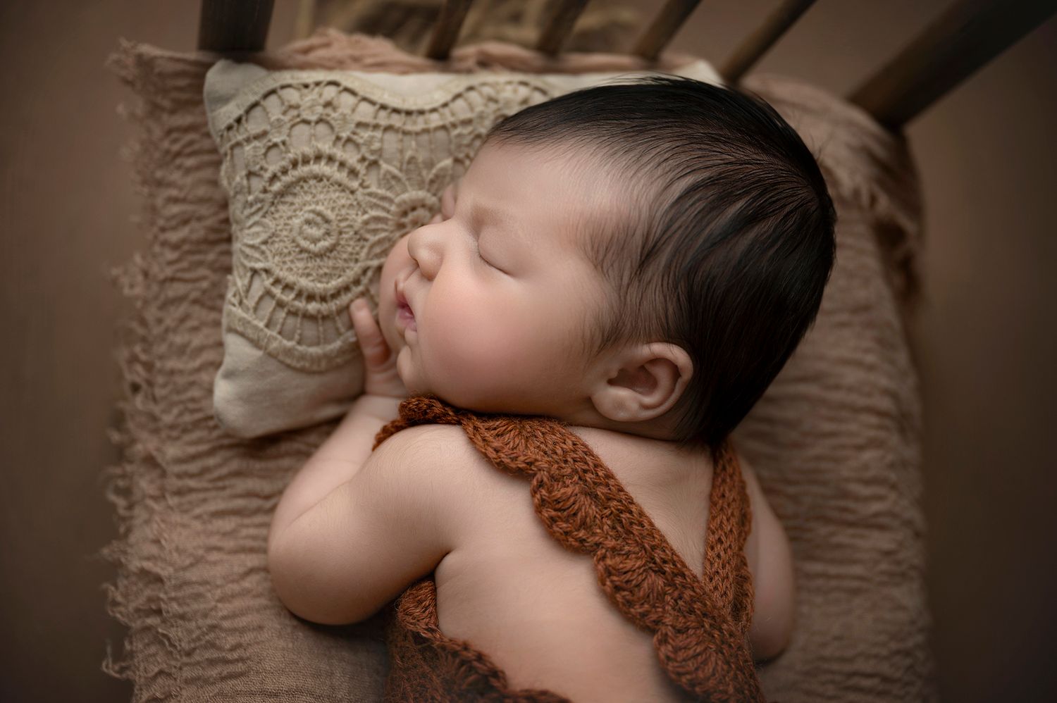 Peaceful newborn baby sleeping on a crochet pillow wearing a brown knit romper.