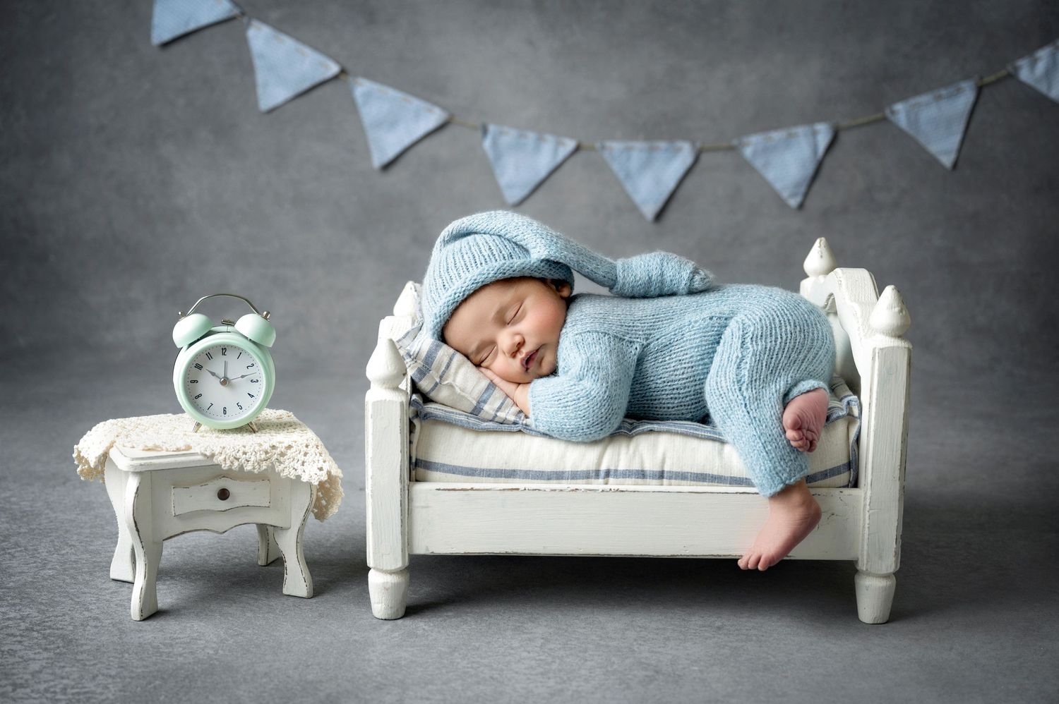 Newborn baby sleeping peacefully in a tiny white bed wearing a blue knit outfit with bunny ears hat.