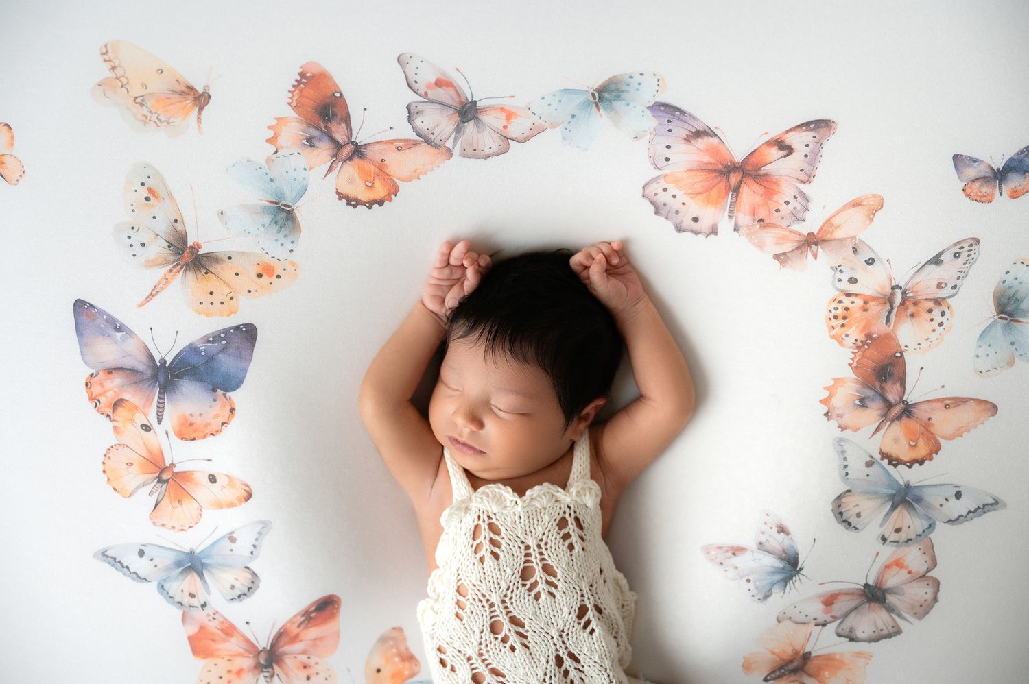 Sleeping newborn baby surrounded by colorful watercolor butterfly decorations on a white background.