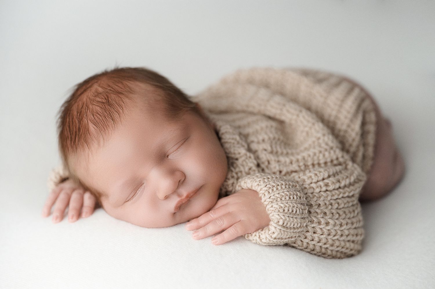 Sleeping newborn baby in beige knit romper on white background.