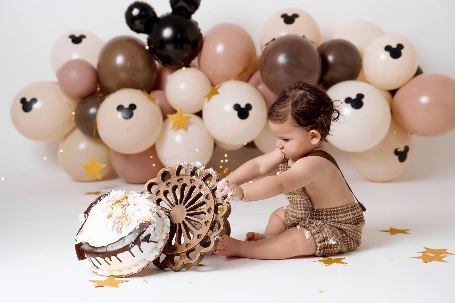 Baby's first birthday cake smash with Mickey Mouse balloons in neutral tones of beige, brown, and black.