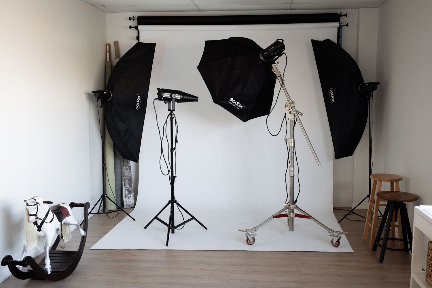 Professional photography studio setup with softbox lights, black backdrop, and equipment on white floor.