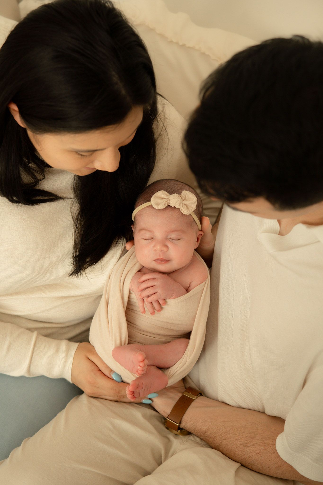 Mum, dad and newborn baby photographed together in a neutral studio.