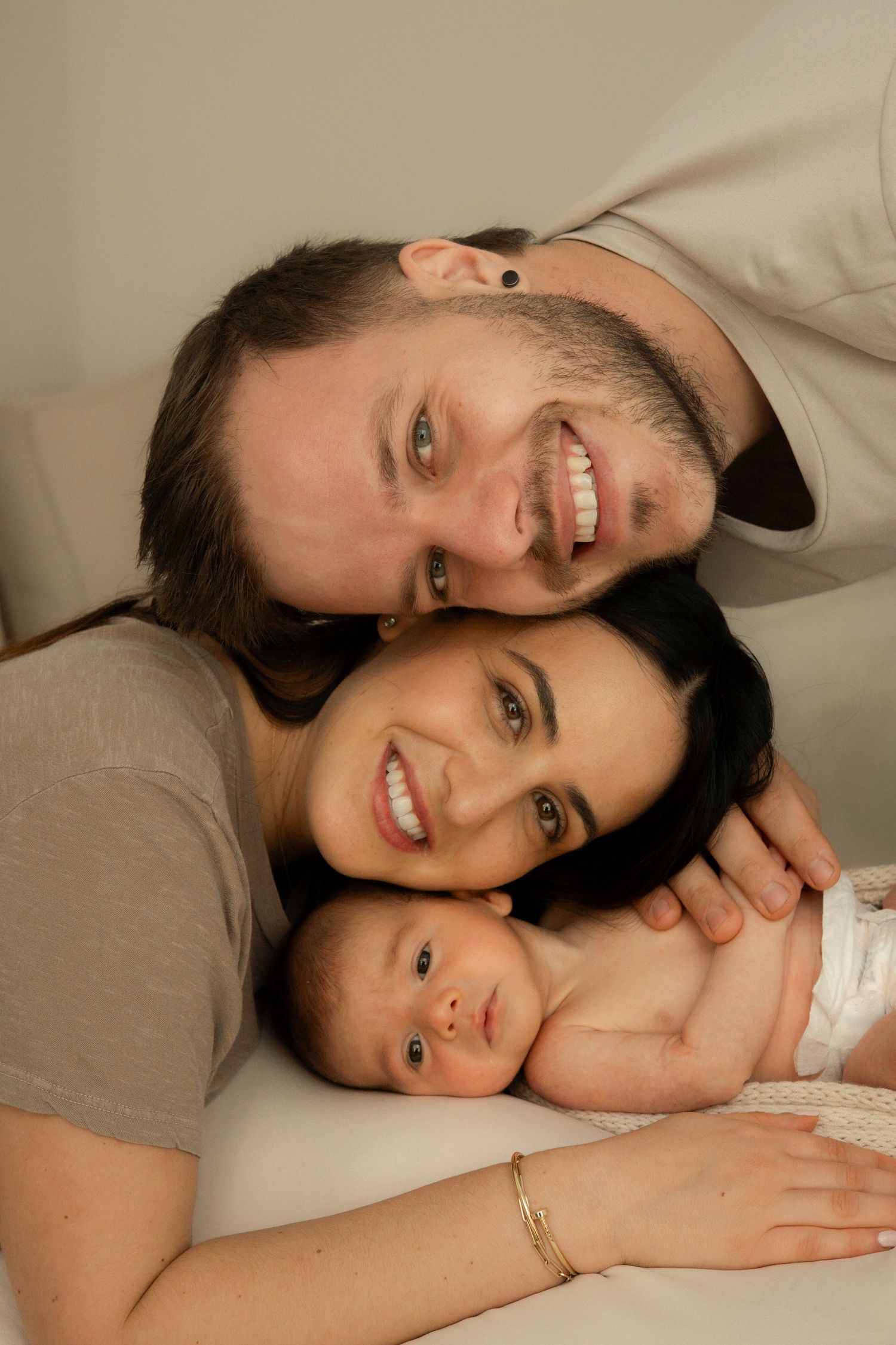 Parents cuddling their newborn in a minimalist photography studio.