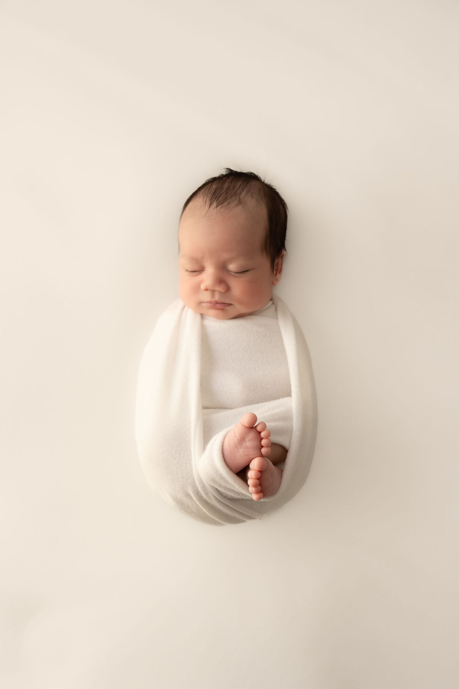 Sleeping newborn wrapped in a cream swaddle in Melbourne studio.