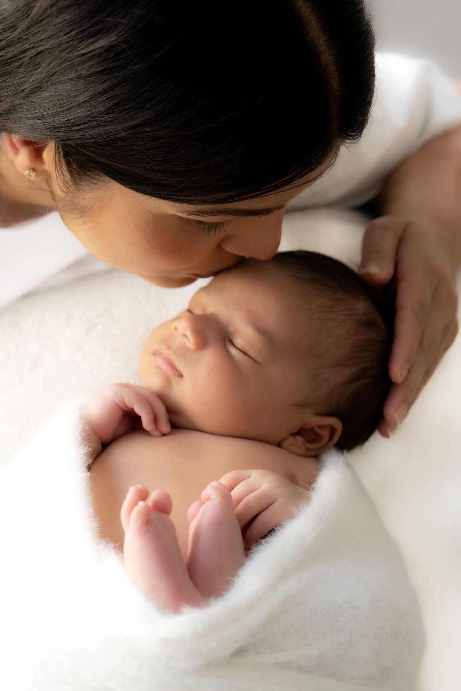 Close-up portrait of a mother and her newborn baby in a minimalist photography studio.
