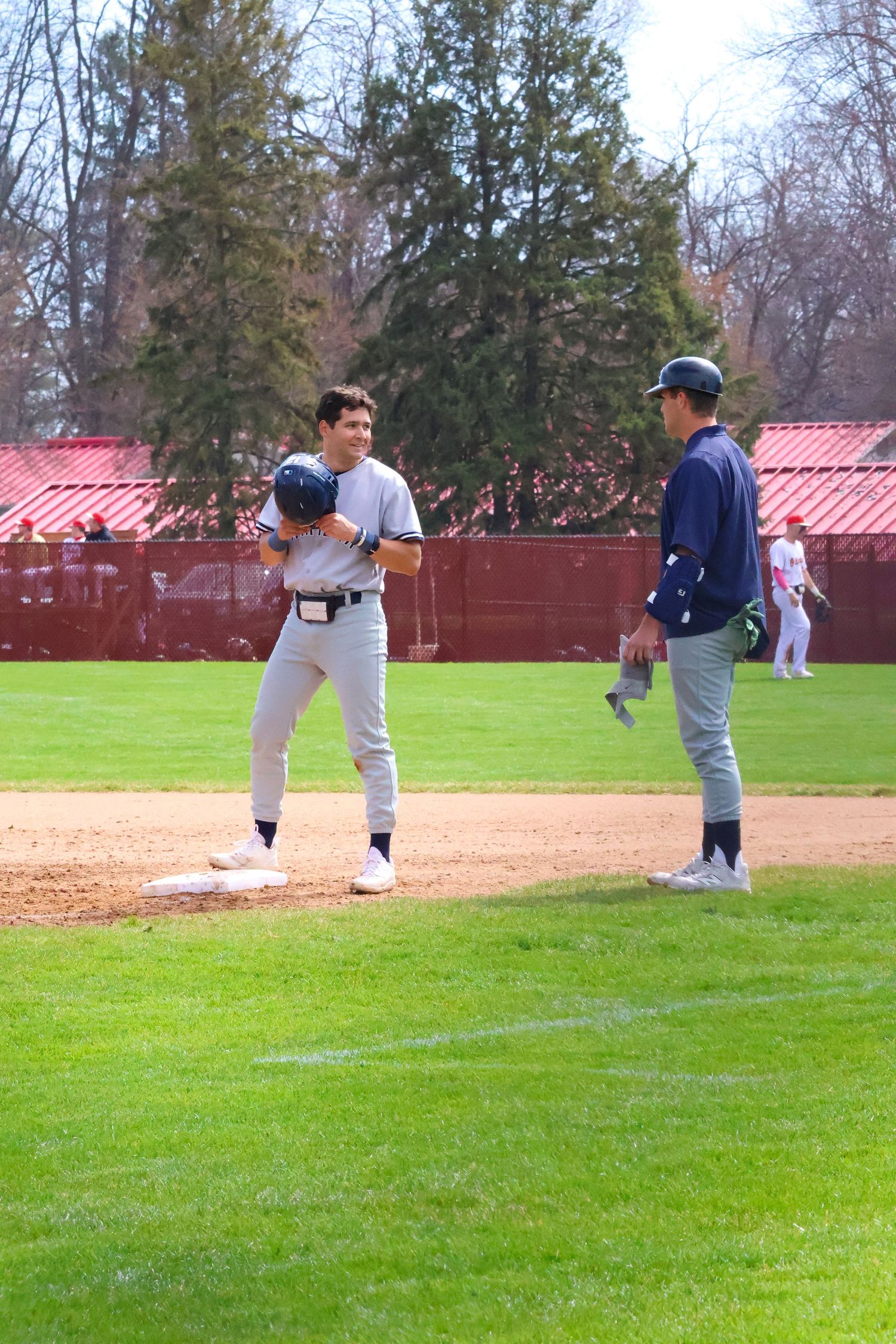 Two Marietta baseball players share a laugh while standing on base during outdoor game.