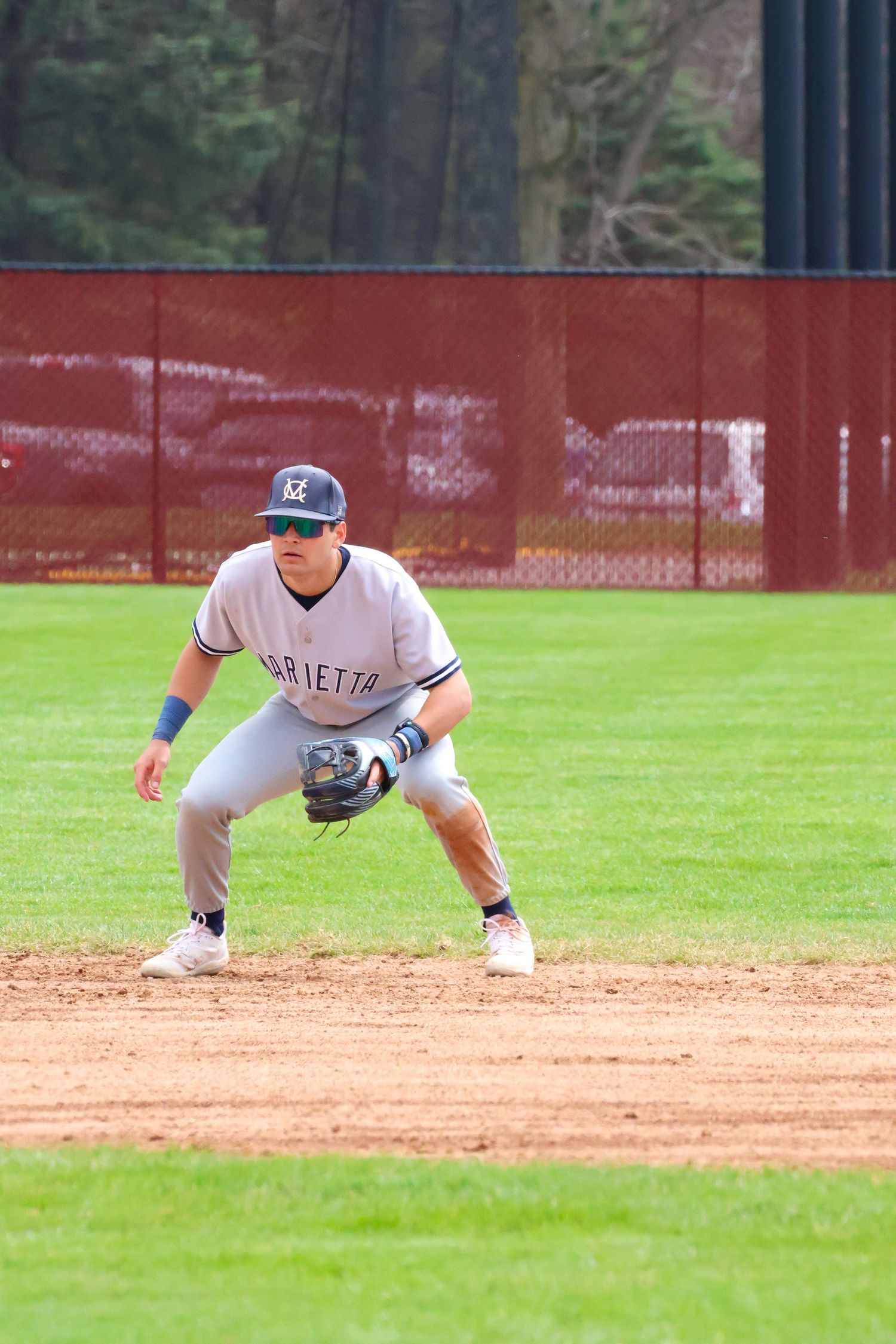 Baseball infielder in Marietta uniform crouches in ready position on dirt infield during game.