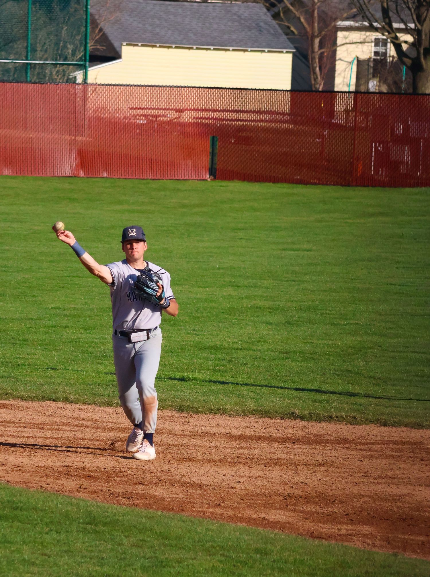 Baseball player in gray uniform winds up to throw ball during outdoor game on dirt infield.