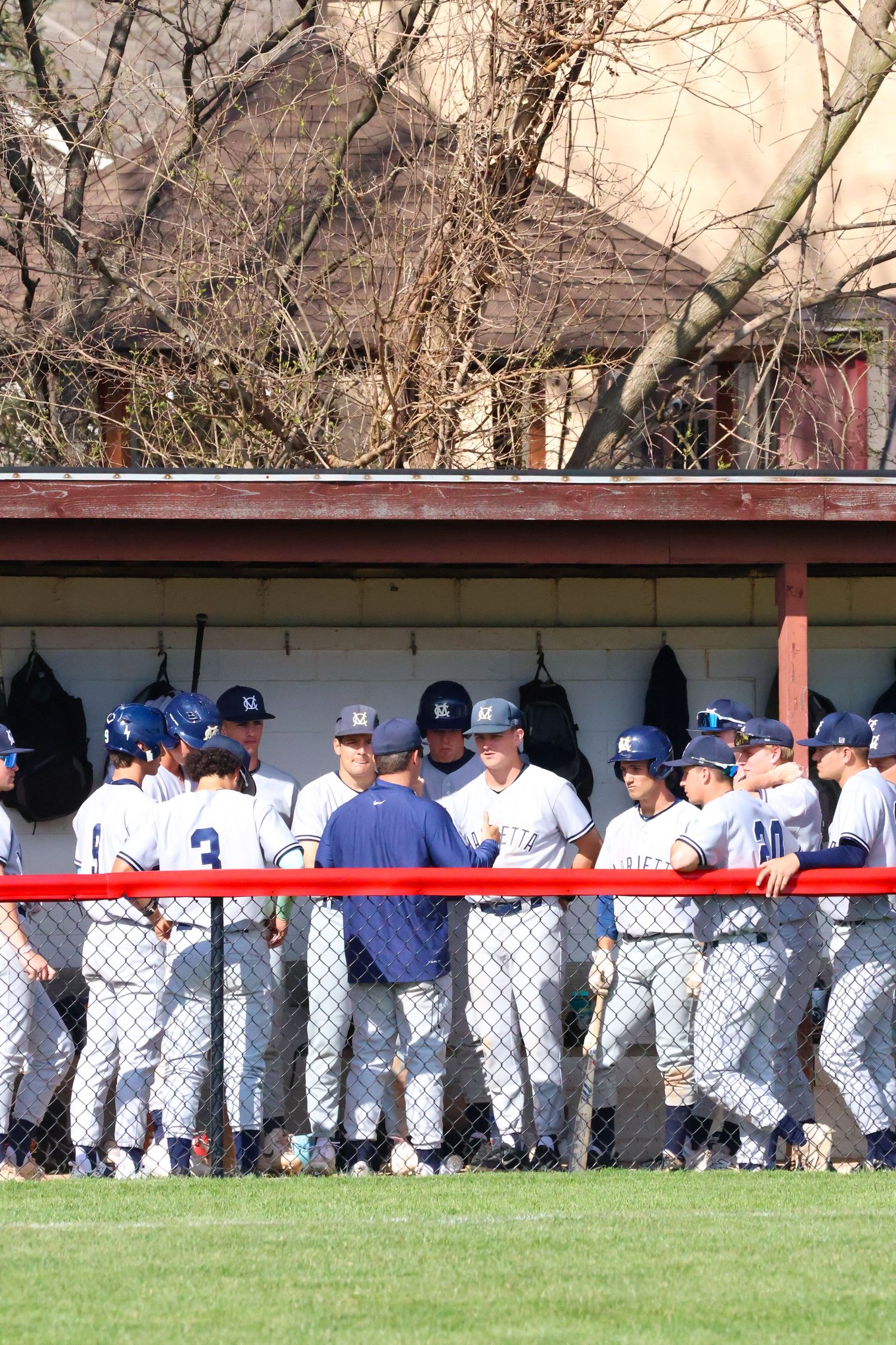 Marietta college baseball team gathers in dugout during game on sunny spring day.