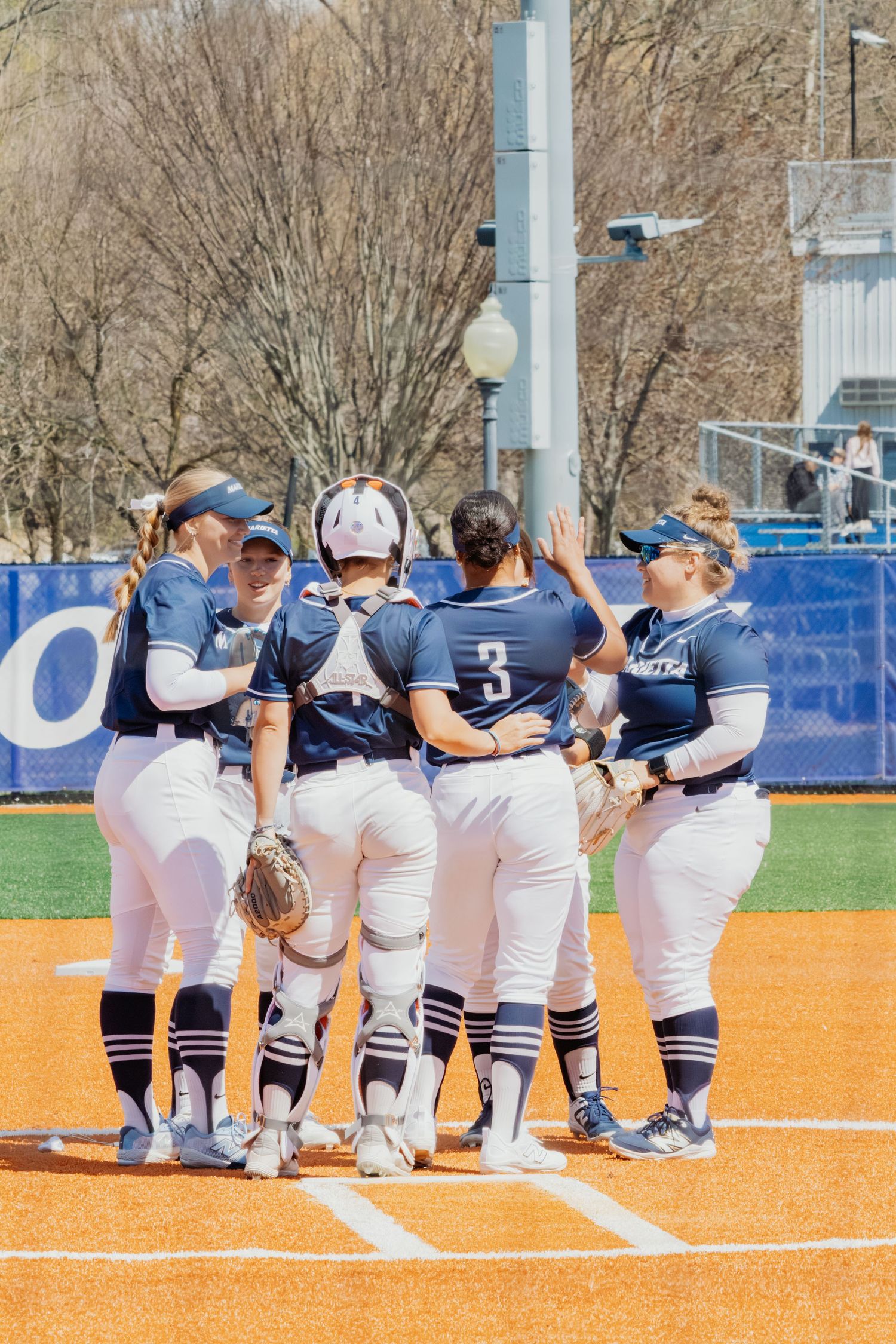 Marietta College softball team huddles on the field during a sunny spring game.