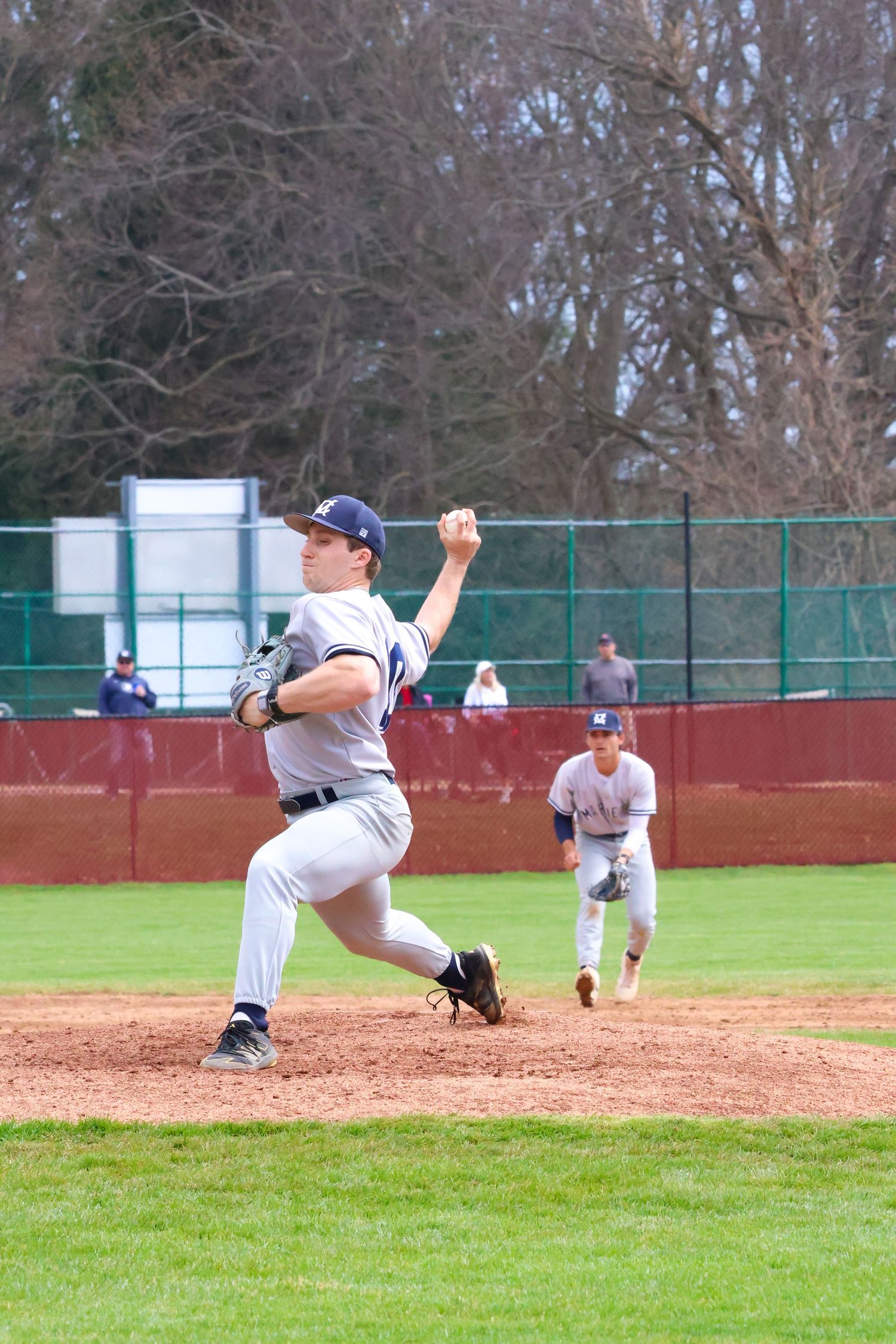 College baseball pitcher in gray Marietta uniform delivers pitch from mound during game.