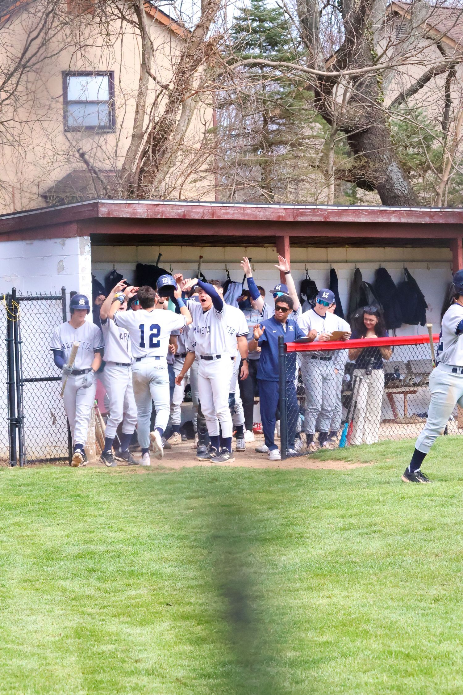 Marietta baseball team celebrates in dugout as player number 12 returns after scoring a run.