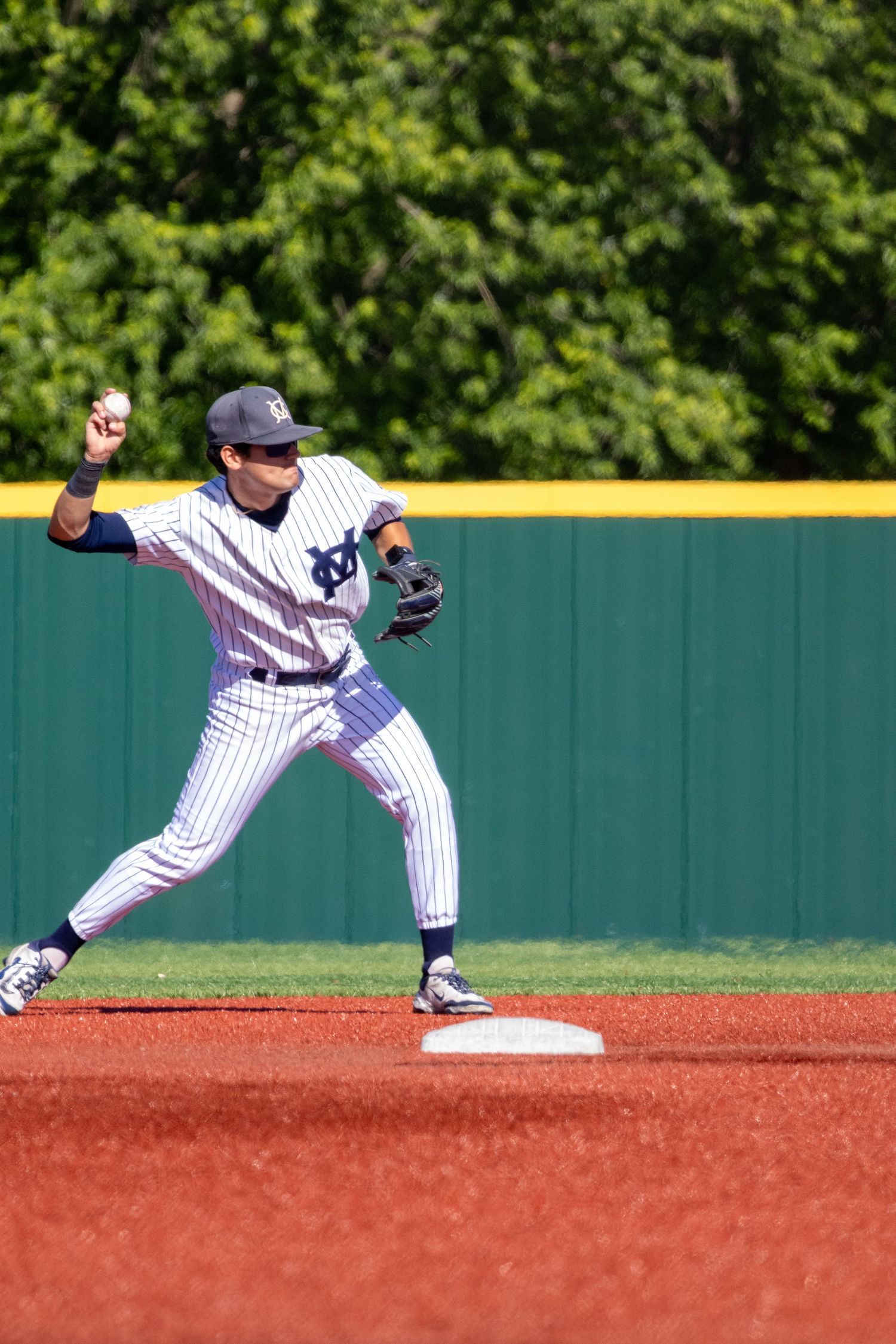 Baseball infielder in pinstripe uniform throwing ball during a game on a sunny day.