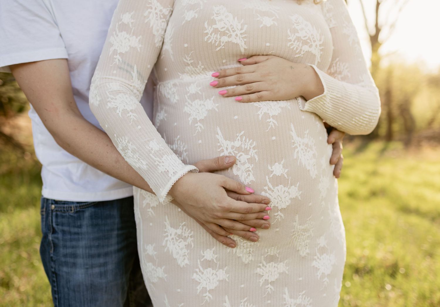 Couple posing for maternity photo shoot outdoors, pregnant woman in floral dress cradling baby bump.