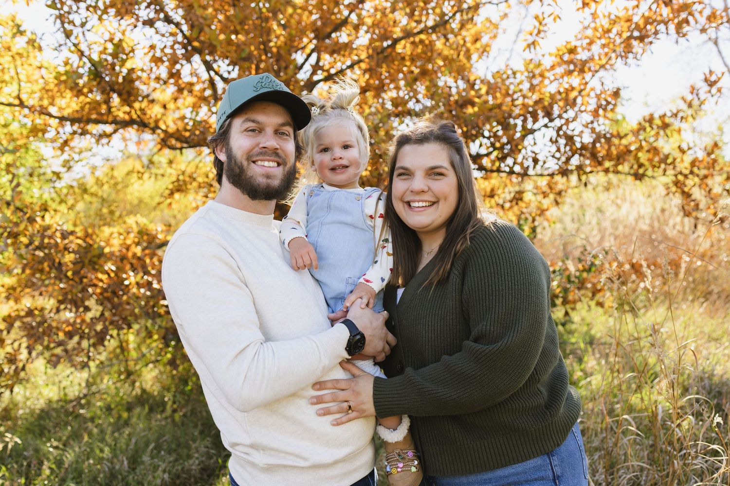 Happy family with baby posing outdoors in autumn foliage setting with colorful fall trees.
