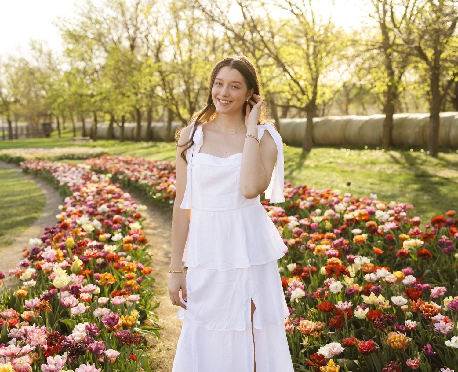 Young woman in white dress smiling among colorful tulip fields in a sunny garden park.
