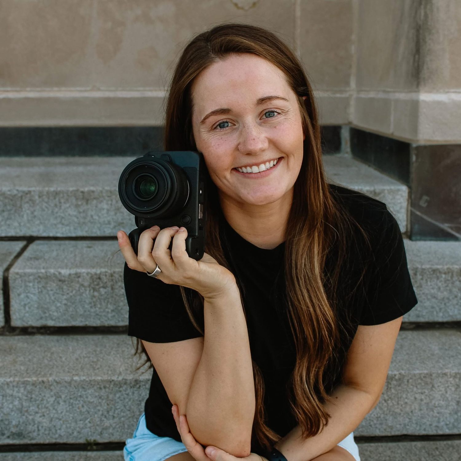 Kaitlyn P. Photography smiling for her branding photos, holding her Canon R6 MarkII up by her face.