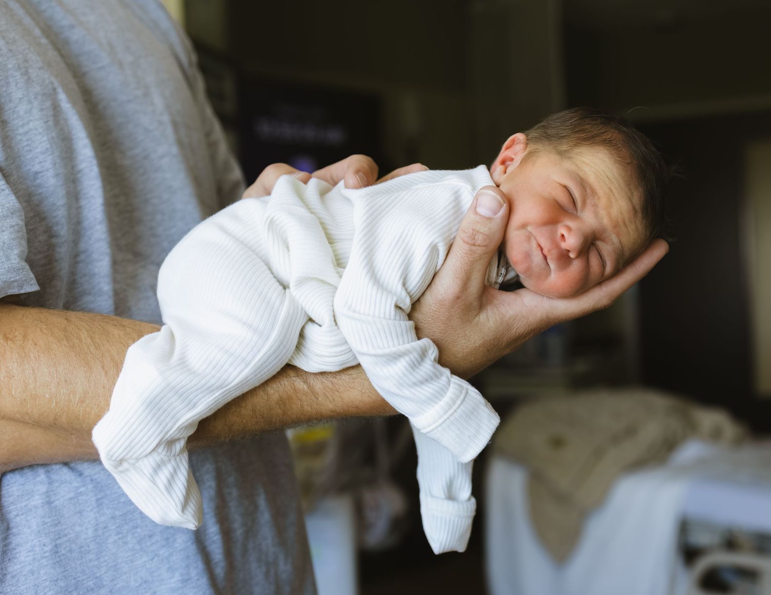 Father holding a newborn baby in a hospital room, cradling the infant gently in one hand.