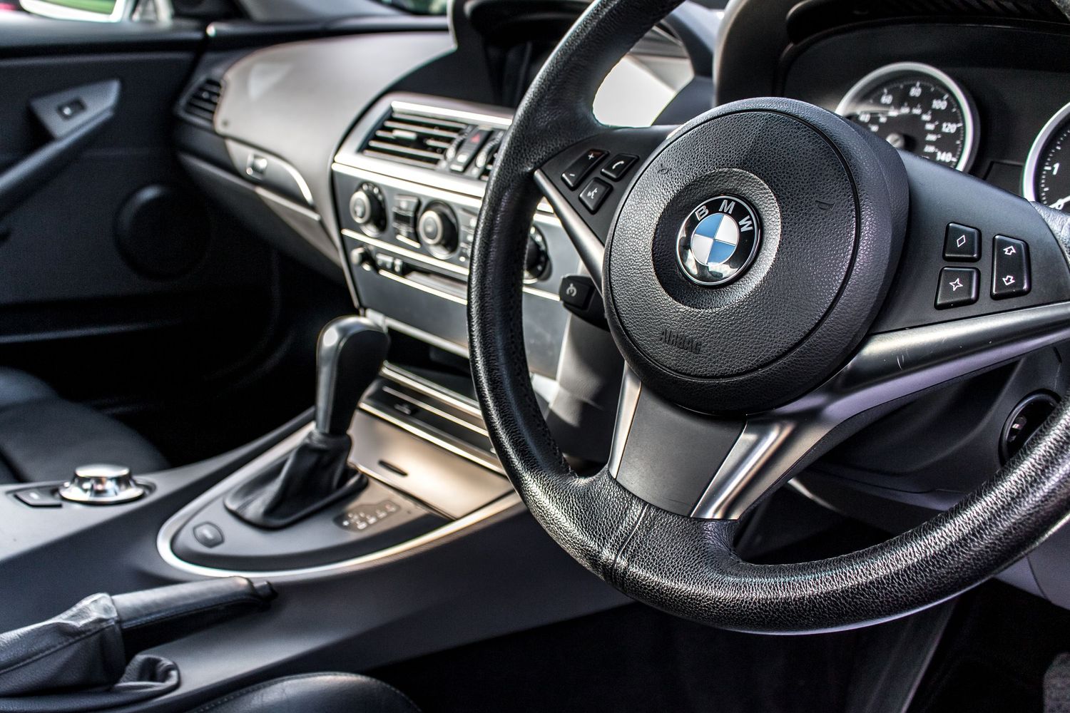 BMW car interior featuring a leather steering wheel, gear shift, and dashboard controls in a right-hand drive vehicle.