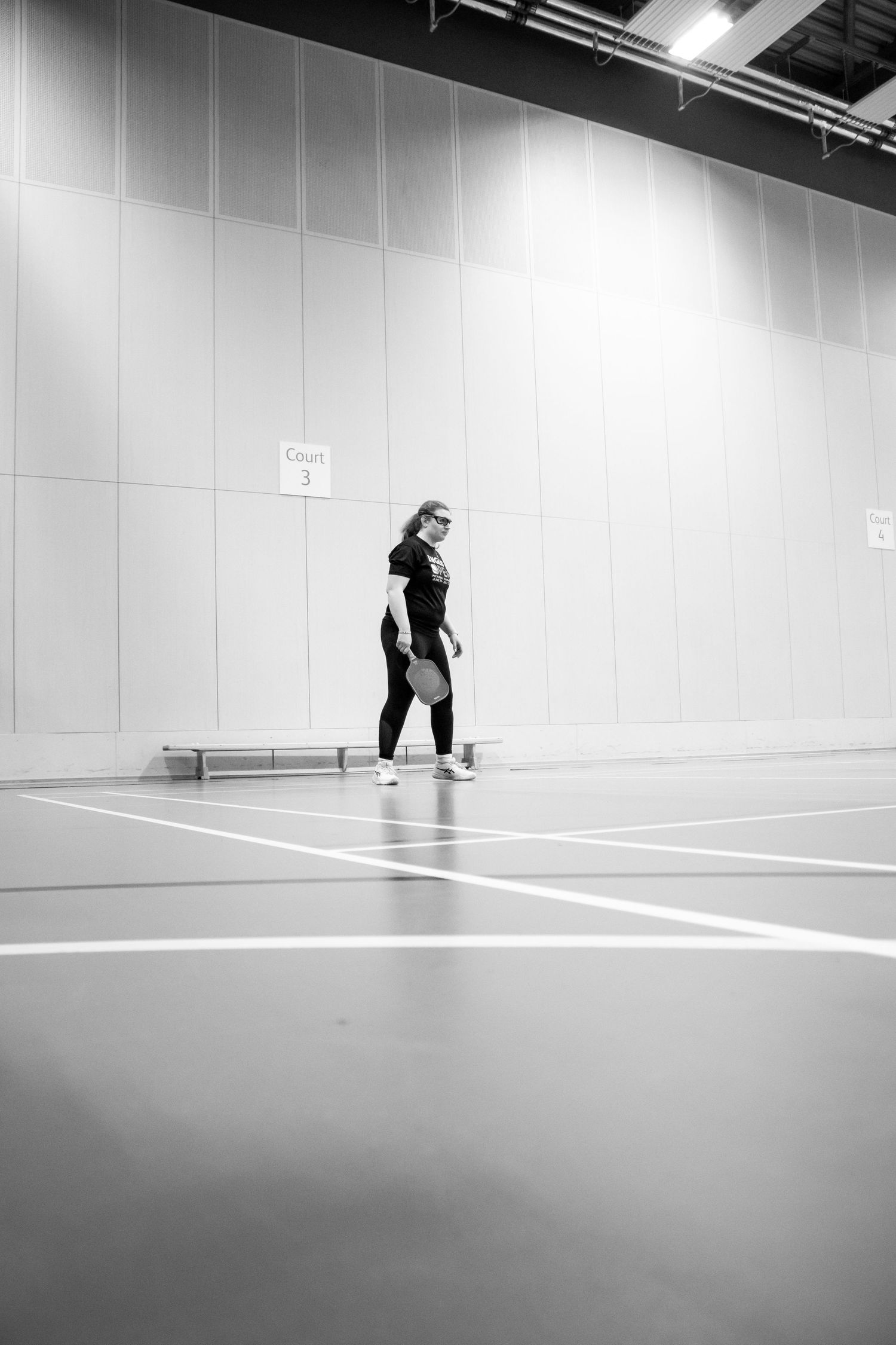 Person exercising alone in a large empty indoor sports hall in black and white.