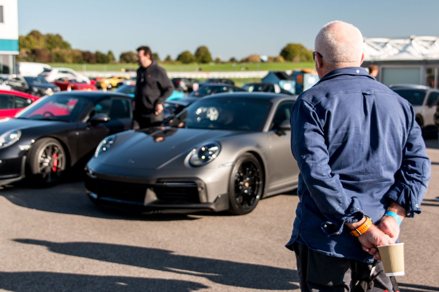 Luxury sports cars lined up at an outdoor event against a sunny sky.