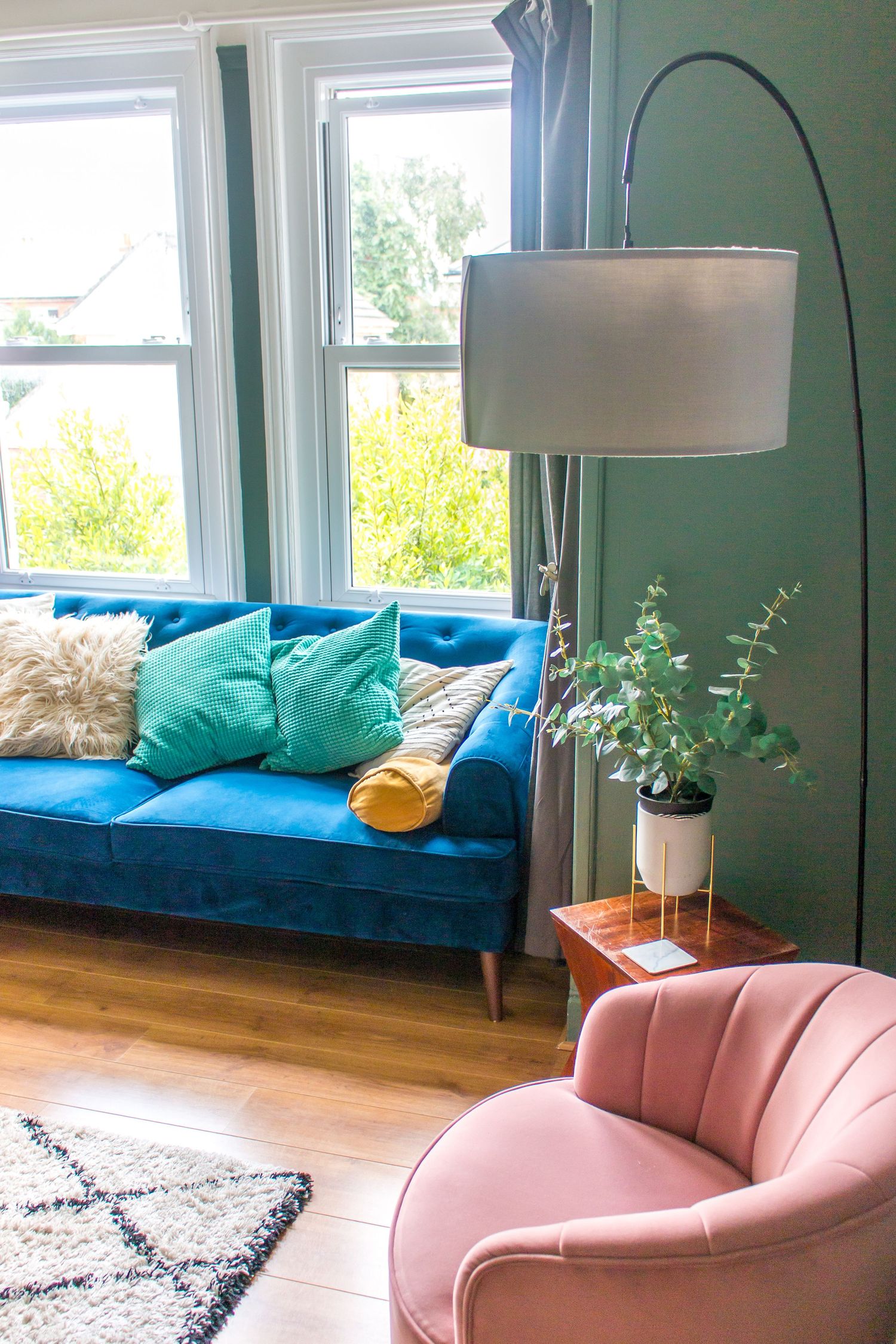 Modern living room with turquoise sofa, pink curved couch, and natural light from large windows.