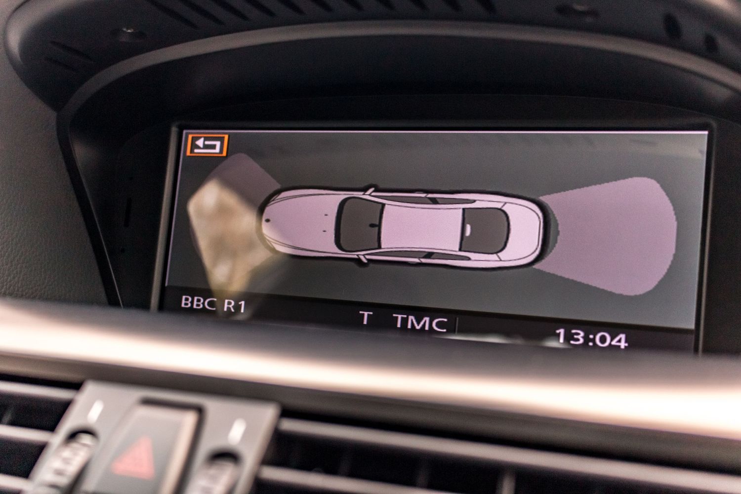 Car backup camera display showing bird's-eye view of vehicle with parking sensors on an in-dash screen.