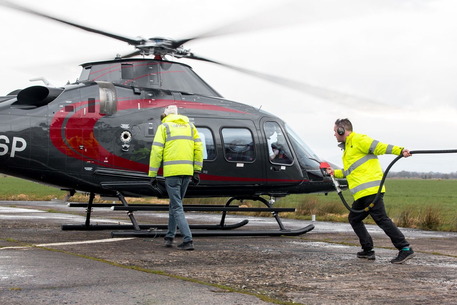 Ground crew in safety vests working around parked helicopters on airfield.
