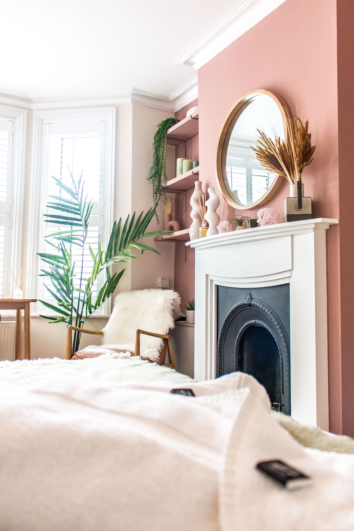 Cozy bedroom with salmon-colored walls, decorative fireplace, and tropical plants.