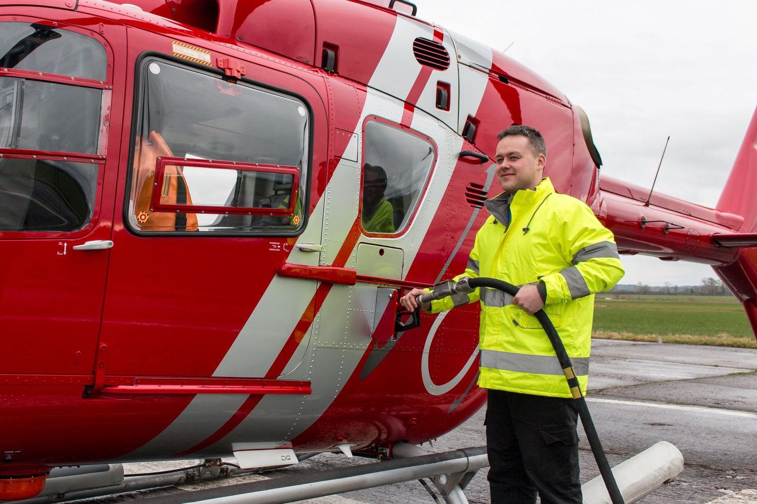 Ground crew performing pre-flight checks on red emergency helicopter.