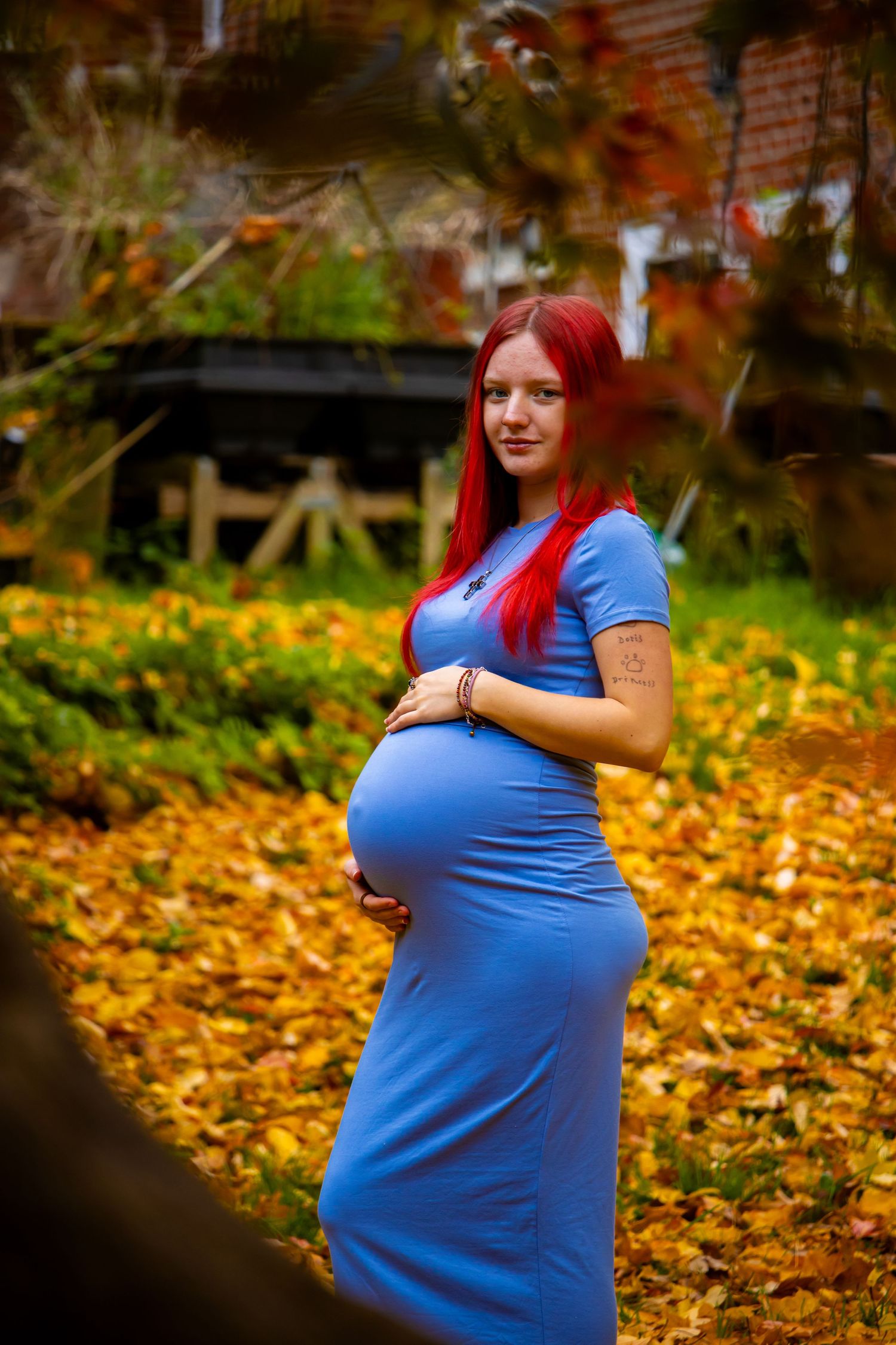 Autumn maternity photoshoot with fallen leaves creating a golden backdrop.