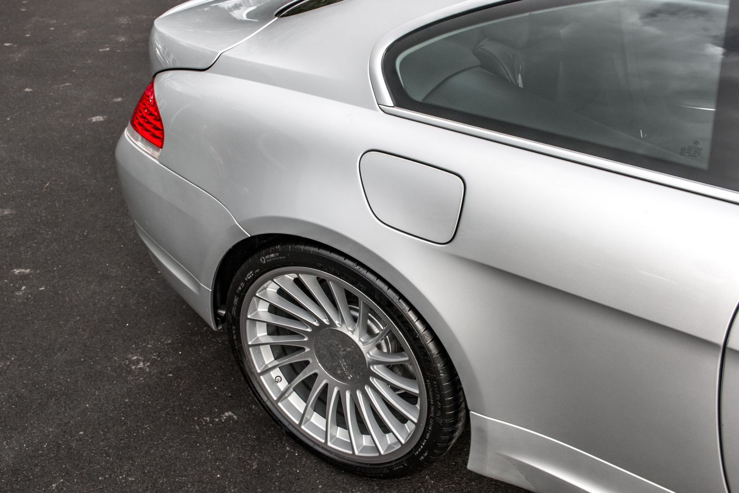 Silver BMW coupe showcasing a multi-spoke alloy wheel and rear quarter panel detail in a parking lot.