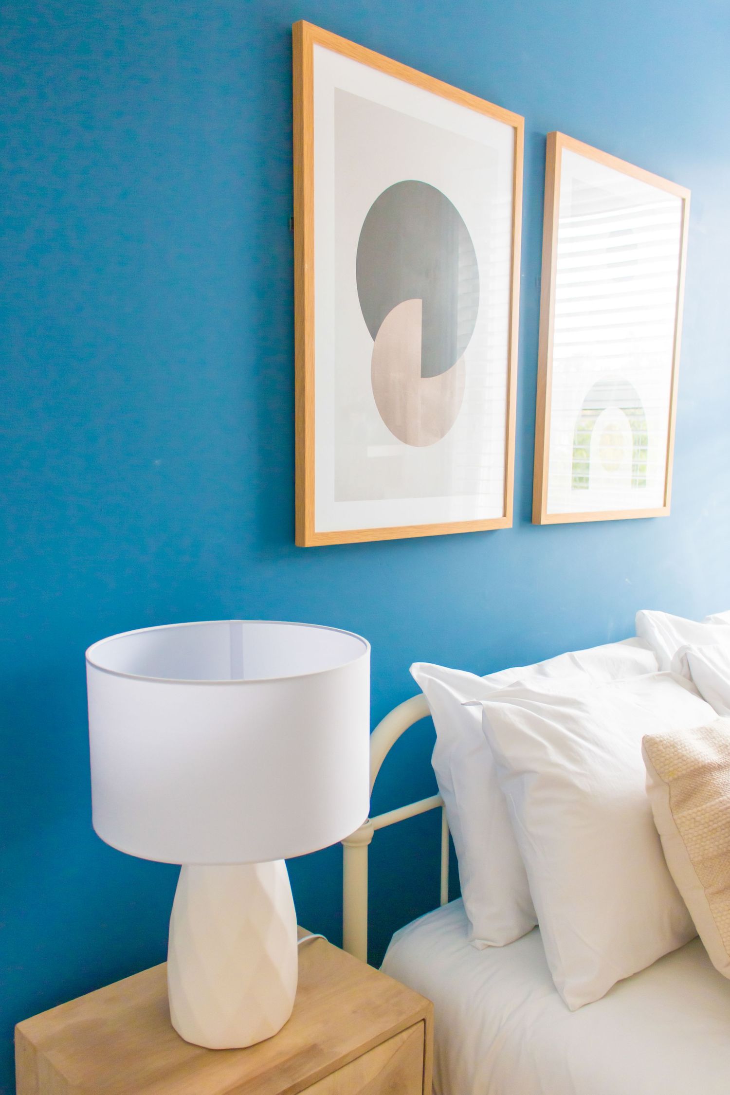 Bedroom with bright blue accent wall, modern white table lamps, and minimalist framed artwork.