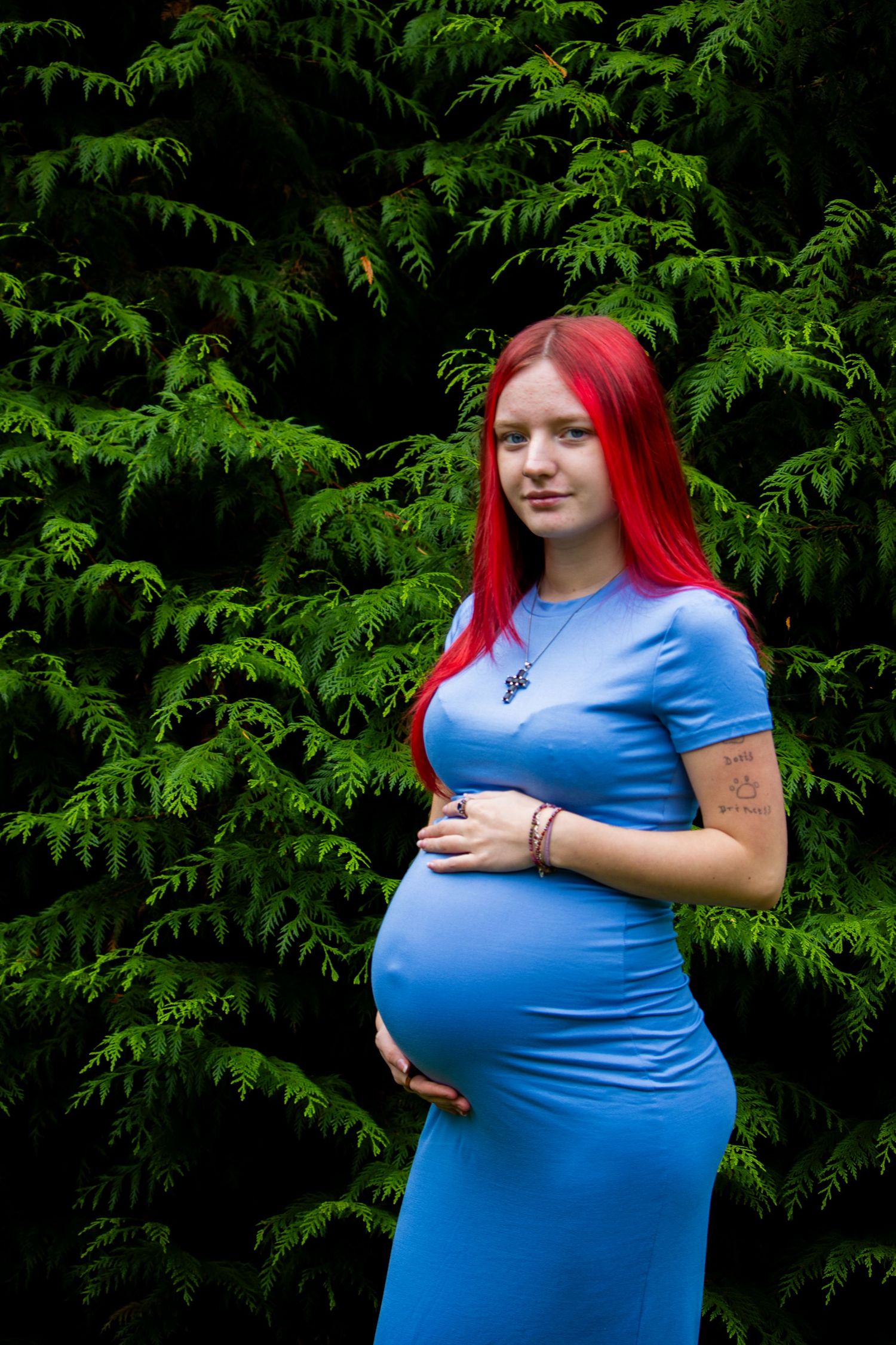 Maternity photos in a garden setting with evergreen trees in the background.