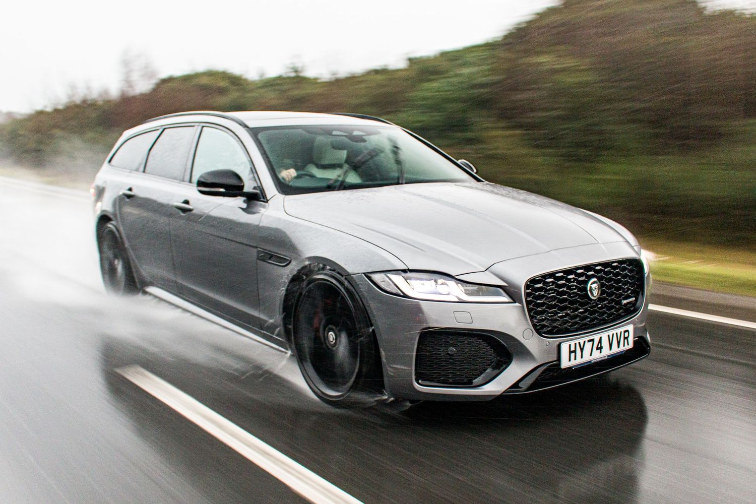 Grey Jaguar XF Sportbrake estate car driving on wet road in rain.