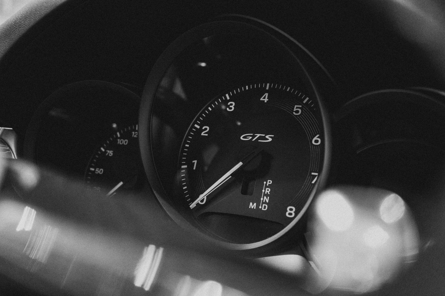 Black and white close-up of a Porsche GTS tachometer dashboard gauge.