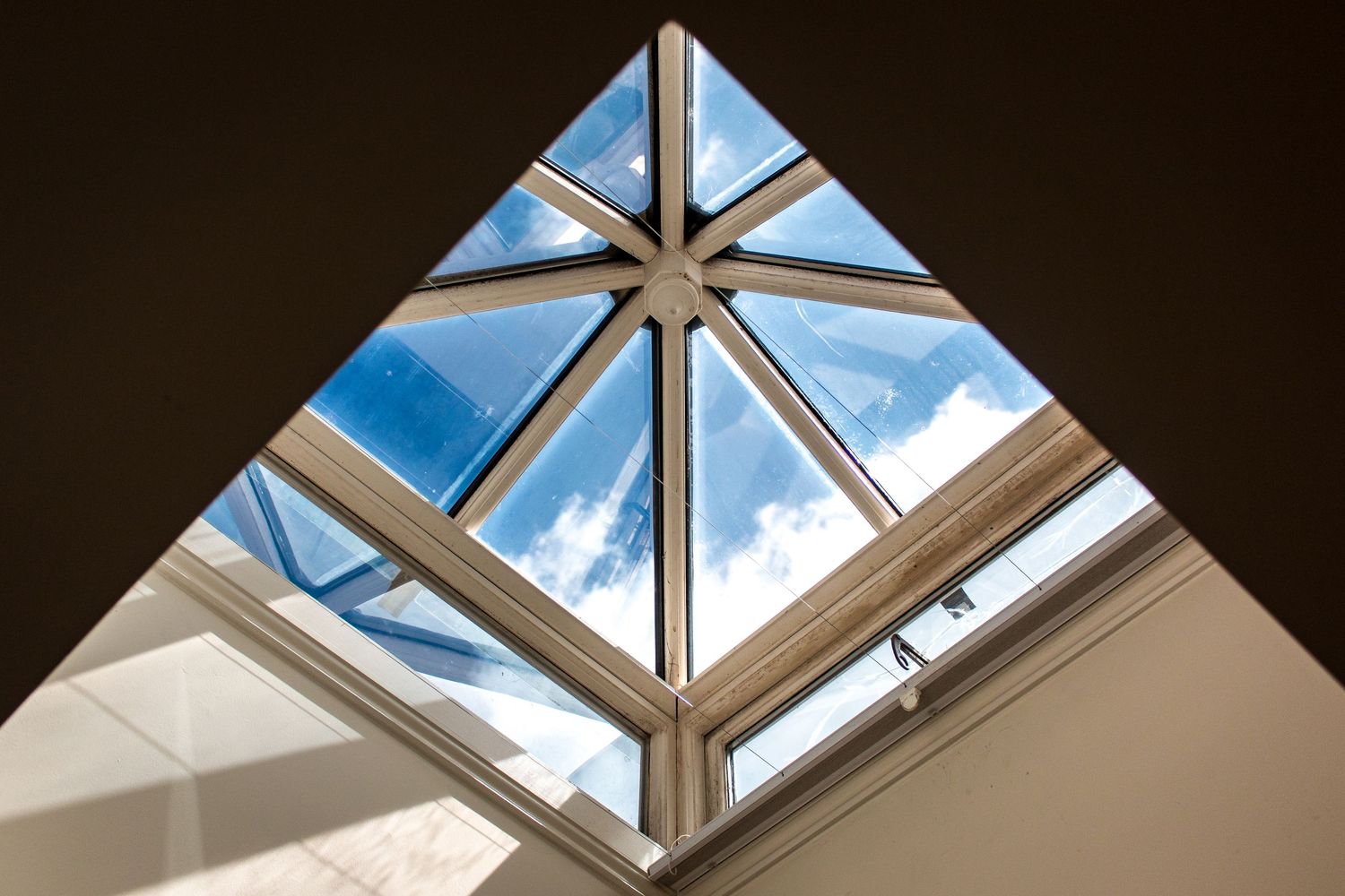 Geometric skylight windows with white frames against a blue sky with clouds.
