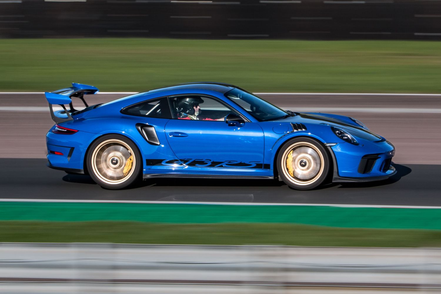 Blue Porsche 911 GT3 RS with gold wheels speeding along a race track, captured with motion blur effect.