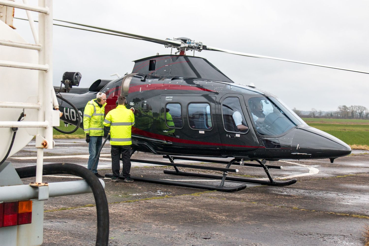 Multiple helicopters parked on wet tarmac with ground support equipment nearby.