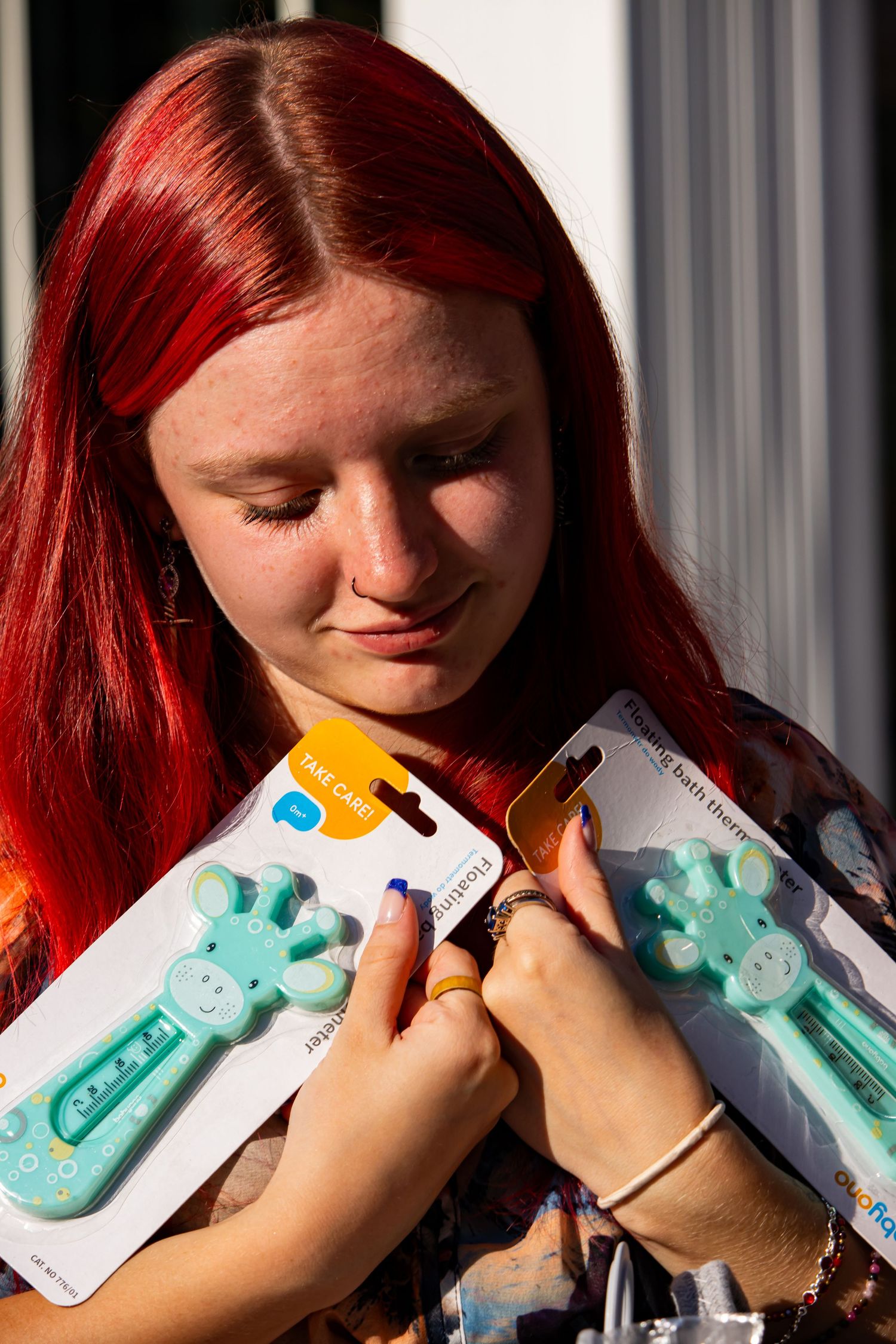 Person with vibrant red hair holding baby toys in sunlight.