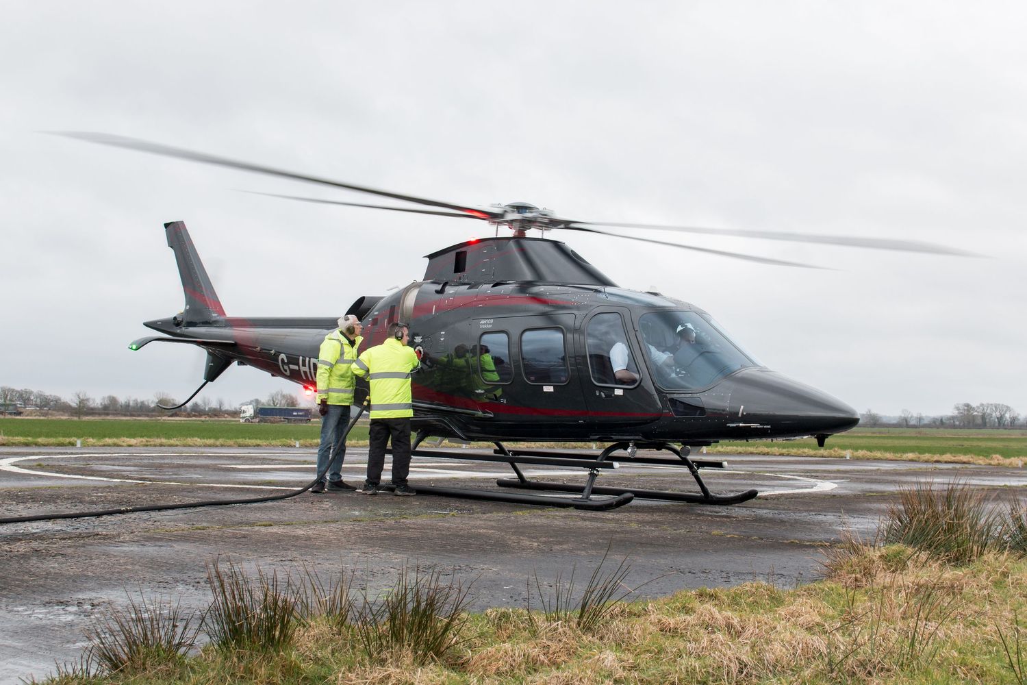 Helicopter on airfield with ground crew in high-visibility vests.