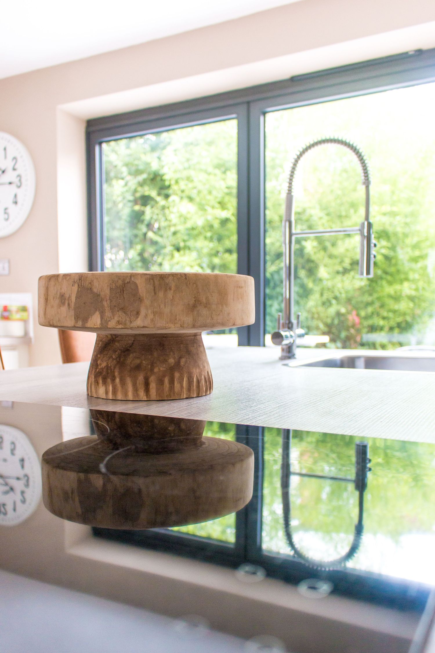 Modern kitchen counter with large windows, wooden accessories, and gooseneck faucet.