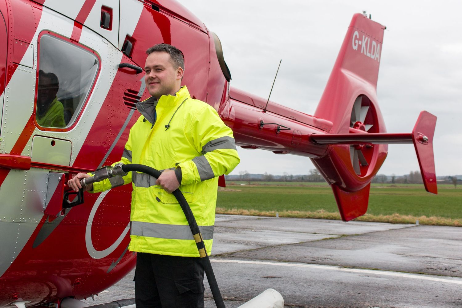 Red helicopter being inspected by maintenance crew in high visibility gear on an airfield.