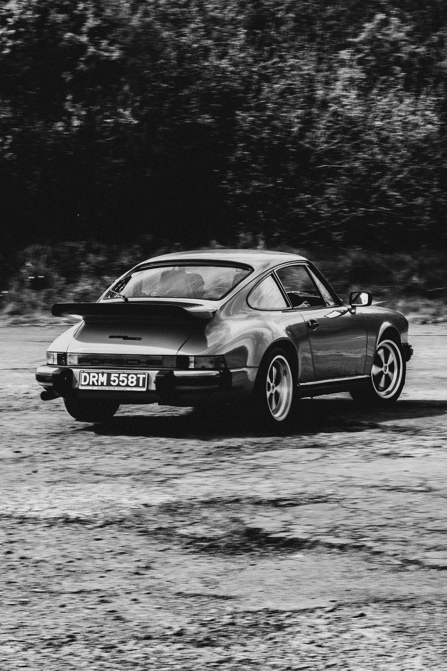 Black and white photo of a classic Porsche 911 Turbo with license plate DRM 558T on a gravel road.