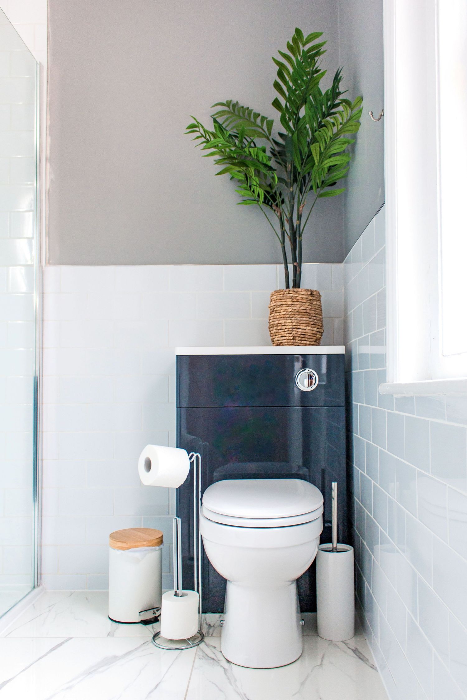 Modern white bathroom with potted plant, toilet and minimalist decor.